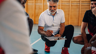 Man with slightly graying hair squats between a group of young men showing them a game board.