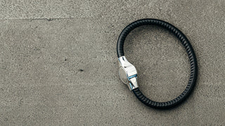 A bracelet with a metal clasp for engraving and a black rubbery band, lays on a cement floor.