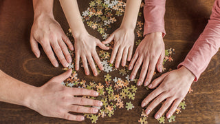close up of a family's hands making a puzzle on a brown wooden table