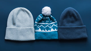 Three winter toques are lined up in a row.  The middle one has a white pompom.  The first is grey, the middle has a blue & white mountain pattern, and the third is a medium blue.
