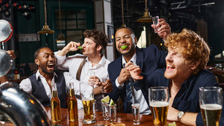 Group of young men gather around a bar with lots of beer glasses, bottles, and shot glasses, to celebrate a bachelor party.