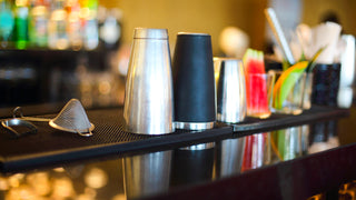 Drink shakers, shot glasses and other drink making accessories sit after being washed on a bar counter top.