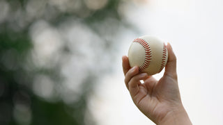 A close up of a hand holding a baseball outside.