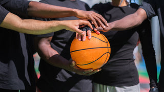 A group of basketball players with their hands over each other, holding a basketball.