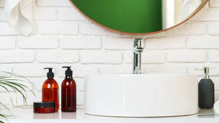 A bathroom sink that is raised with a white brick background, surrounded by 3 soap dispensers.