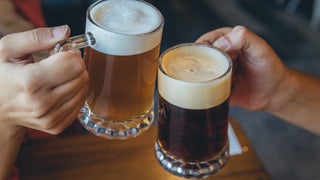 Close up of two people cheers-ing with glass beer mugs full of different shades of beer