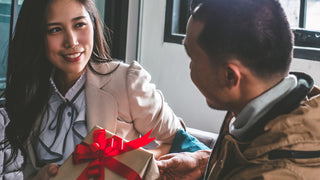 Young Woman with brown hair in a cream coloured business jacket is receiving a wrapped gift from a young man.