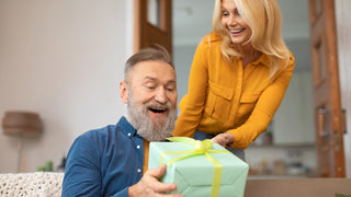 Older man with greying beard receives a gift from his wide with medium length blonde hair.