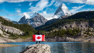 Beautiful Mountain Landscape like the Rockies with a girl standing with her back to the camera holding a Canadian flag.