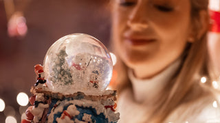 Woman in turtleneck holds a snow globe out towards the camera.