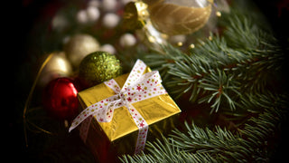 Christmas gift wrapped in gold paper and a bow sitting on a Christmas tree with Christmas ornaments