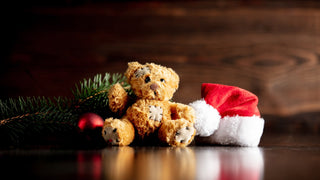 Small brown stuffed bear sits with a Santa hat and some evergreen branch on a wooden table