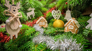 Wooden Christmas tree ornaments sit on a decorated Christmas tree with garland.  Ornaments are reindeer, gingerbread houses, bells, hearts.