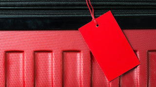 A close up of a red suitcase with a blank red luggage tag hanging off the bag.