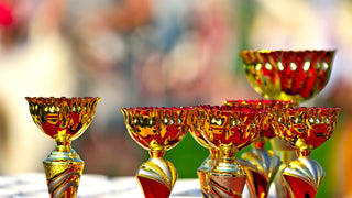 A group of several gold trophy cups with gold designs and a bit of red.