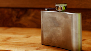 A metal flask sits on a wooden table or bar.