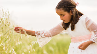 Girl in white lace communion dress plays with flowers outside.