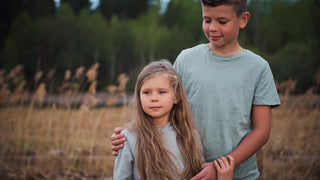 Brother and Sister have a little side hug while walking in a field of long dry grass.