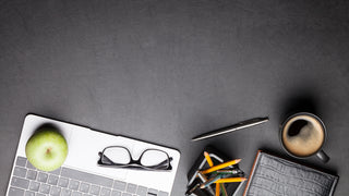 Black Desk with a laptop, apple, glasses, ceramic coffee mug, pencils, pencil holder, on a desk.