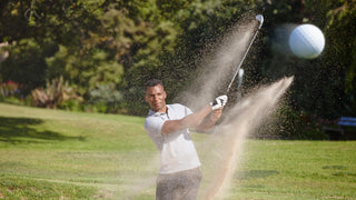 Man hitting a golf ball through sand