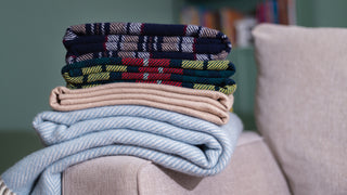 A stack of warm blankets with various patterns, stacked on a beige couch arm rest.