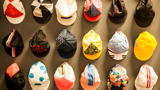 3 rows of baseball hats in an assortment of designs and colours are hanging on a wall.