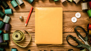 Leather Notebook on a wooden table surrounded by craft supplies.  Can be customized with a logo or text.