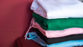 A stack of various coloured sweatshirts sit against a deep red background.