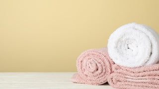 A stack of white and pink towels with 2 rolled up on top, sit on a white table with a yellow background.