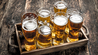 An assortment of beer pint glasses are served in a rustic wooden tray.