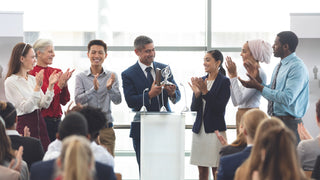 Group of various business people standing in front of an audience while one person hands out an employee recognition award