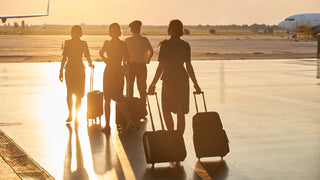 Group of travellers walk into the sunset on a tarmac with assorted luggage.