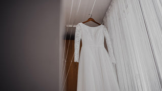 White long sleeved wedding dress hanging on a dark wooden hanger