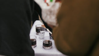 View through two people at a wedding of a table with a white tablecloth and whisky and shot glasses sitting on it