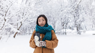 Woman outside in the winter with a blue scarf and beige puffer jacket holding a travel coffee mug