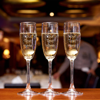 3 Champagne Glasses sit on a bar.  They have space to add a custom message.