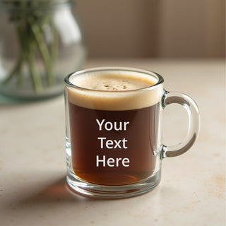 Glass Coffee mug with round handle sits on a counter with a space for white custom engraving on the front.