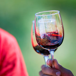 2 people are cheers-ing, using custom red wine glasses with stems with a space on the front for a custom message.